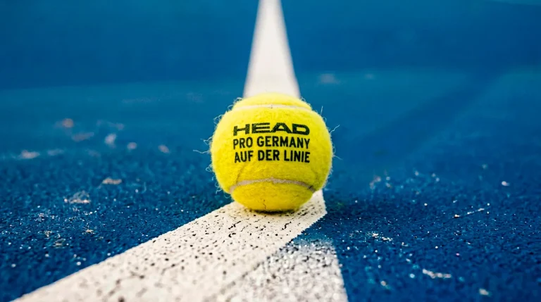 Tennis Wettarten erklärt — Nahaufnahme eines Tennisballs auf der Linie eines Hartplatzes bei Flutlicht